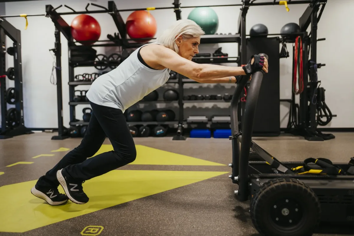 An older member drives a wheeled sled across the training floor at Alloy Personal Training Royal Oak in Royal Oak, MI.