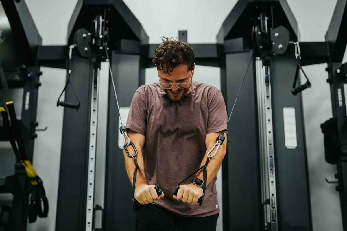A member presses through a cable crossover on a dual-stack machine at Alloy Personal Training Royal Oak in Royal Oak, MI.