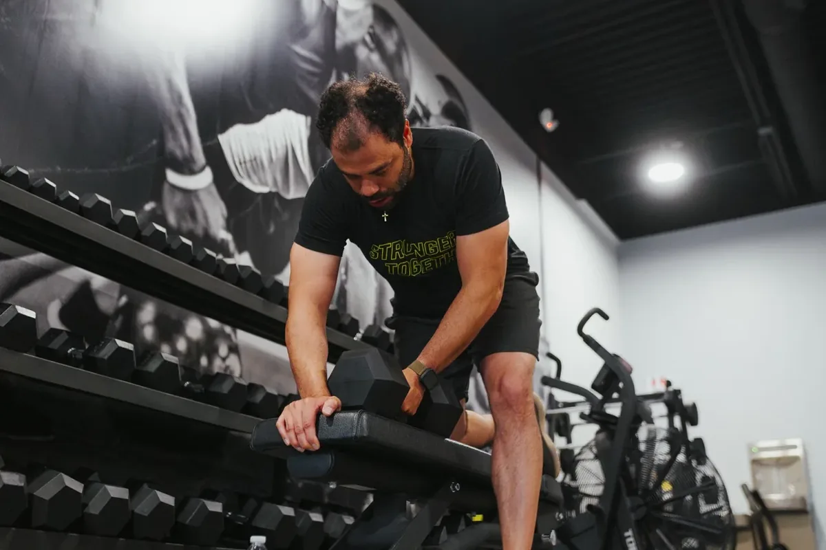 A member sets up a dumbbell on an incline bench beside the dumbbell rack at Alloy Personal Training Royal Oak in Royal Oak, MI.