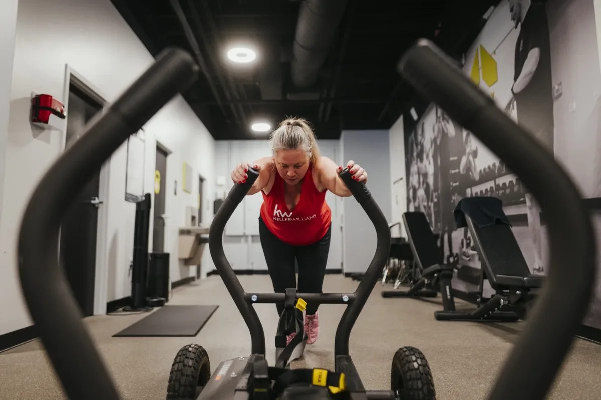 A member pushes a tank sled head-on down the gym floor during a conditioning block at Alloy Personal Training Royal Oak in Royal Oak, MI.
